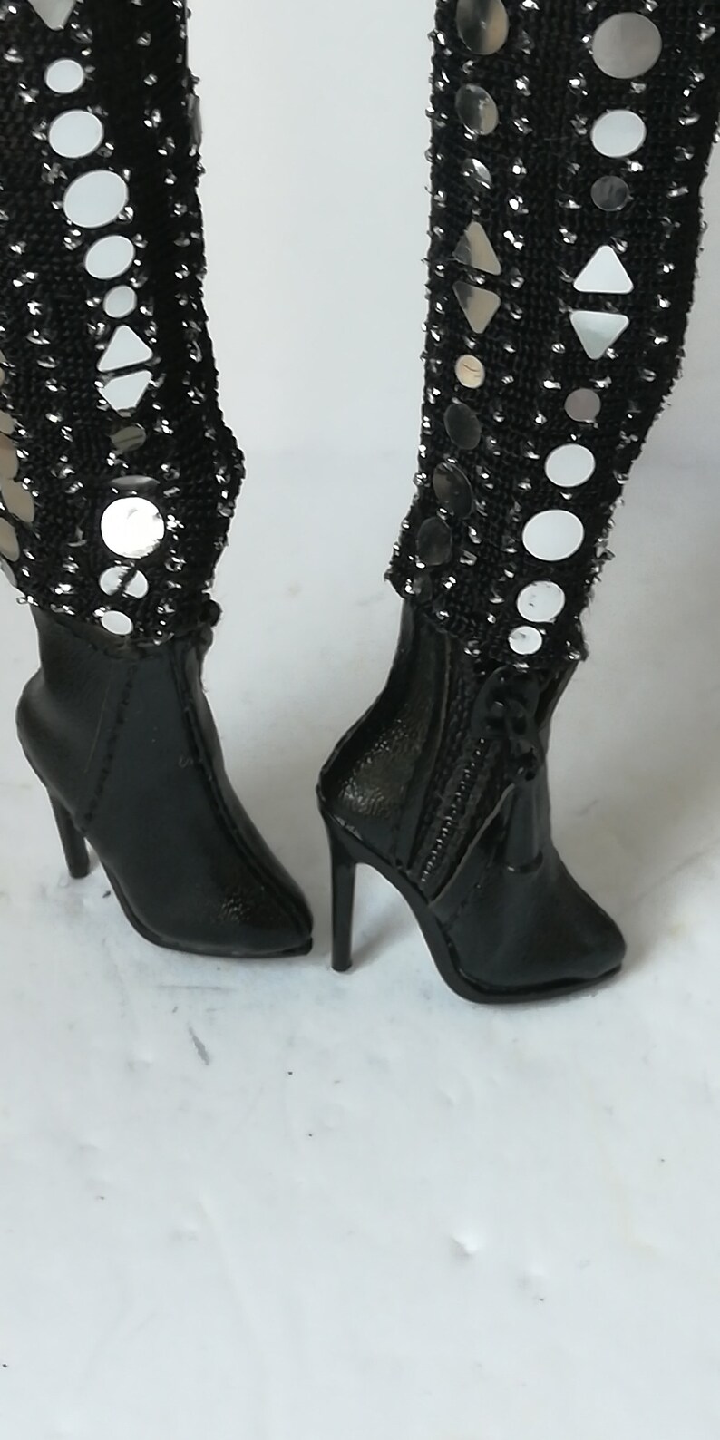 May include: A pair of black heeled boots with a zipper up the back. The boots are decorated with silver sequins and mirrored circles.