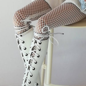 May include: White lace-up boots with a peep toe and a high heel. The boots are worn with white fishnet stockings.