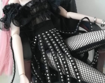 May include: A fashion doll wearing a black hat, a black lace top, a black skirt with silver embellishments, and black fishnet stockings. The doll is sitting on a black office chair.