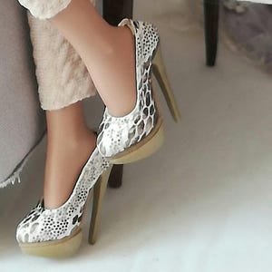 Könnte beinhalten: Ein Paar High-Heel-Schuhe mit Schlangenhautmuster. Die Schuhe sind weiß mit braunen Akzenten und haben eine beige Plattform.