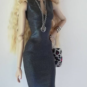 May include: A doll wearing a grey dress with a silver chain necklace featuring a heart pendant that says "LOVE". The doll has blonde hair and is wearing sunglasses.