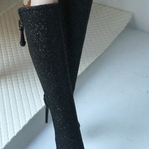 May include: A pair of black sparkly high-heeled boots with a pointed toe and a small bow detail on the side.