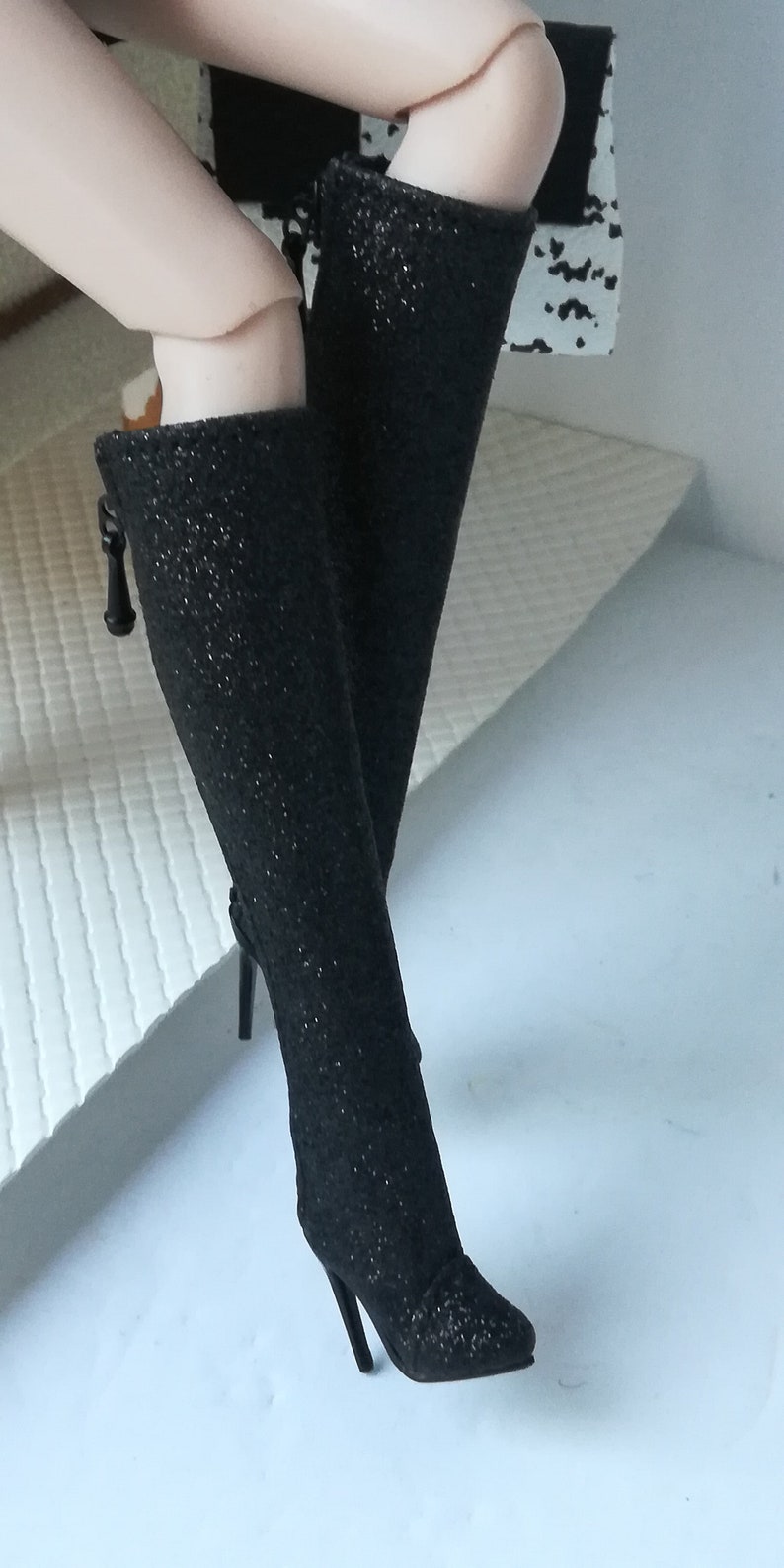 May include: A pair of black sparkly high-heeled boots with a pointed toe and a small bow detail on the side.