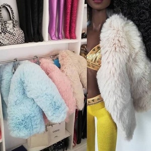 Puede incluir: Cuatro chaquetas de piel sint&eacute;tica de diferentes colores colgadas en un perchero. Las chaquetas son azul claro, rosa, crema y blanca. Las chaquetas son todas esponjosas y suaves.