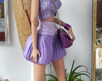 May include: A purple and silver doll with lavender hair wearing a purple crop top, matching shorts, and purple boots. The doll is holding a purple purse and has silver earrings with purple accents.