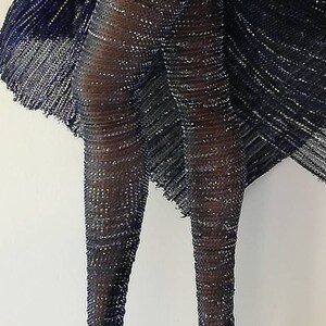 May include: A pair of black fishnet stockings with silver glitter. The stockings are worn on a model's legs and are shown from the front.