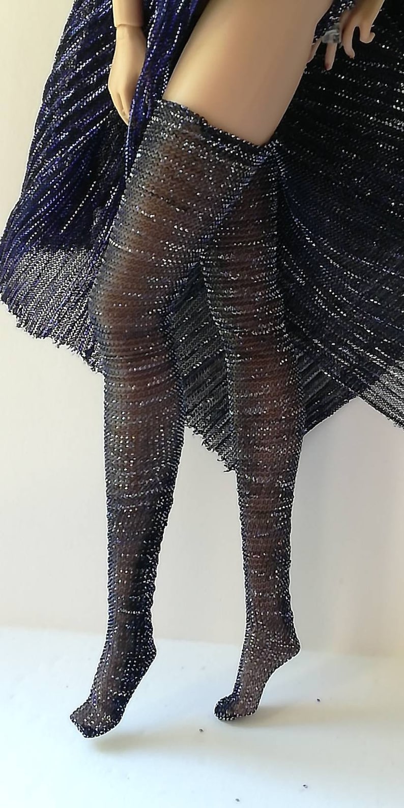 May include: A pair of black fishnet stockings with silver glitter. The stockings are worn on a model's legs and are shown from the front.