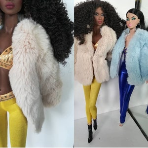 May include: Two dolls wearing faux fur jackets. One doll is wearing a light blue jacket and blue trousers. The other doll is wearing a cream coloured jacket and yellow trousers.