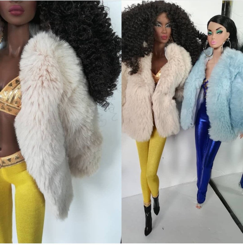 May include: Two dolls wearing faux fur jackets. One doll is wearing a light blue jacket and blue trousers. The other doll is wearing a cream coloured jacket and yellow trousers.