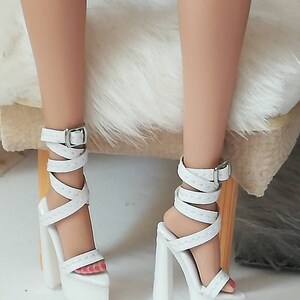 May include: White platform sandals with a thick strap and buckle. The sandals have a white platform and a white heel.