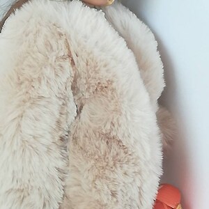 Puede incluir: Una mu&ntilde;eca con un abrigo de piel sint&eacute;tica de color crema, medias estampadas en negro y naranja y un peque&ntilde;o bolso de mano naranja. La mu&ntilde;eca lleva gafas de sol redondas grandes.