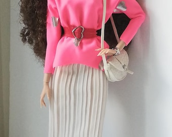 Può includere: Bambola alla moda con un top rosa a maniche lunghe con dettagli a cuore argentati, una cintura rossa e una gonna plissettata bianca. La bambola porta una borsa bianca e indossa orecchini argentati e scarpe bianche e nere. La bambola ha lunghi capelli castani ricci.
