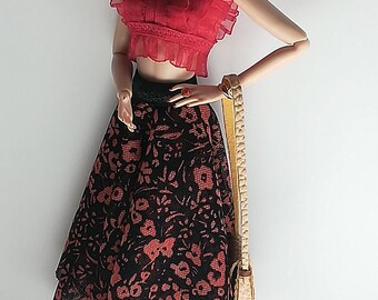 May include: A fashion doll wearing a red ruffled crop top, a black and red floral skirt, black sandals, and sunglasses. The doll is holding a tan handbag.