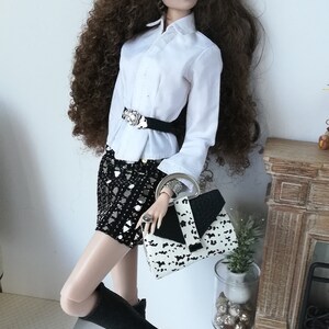 May include: A doll wearing a white button-down shirt with a black belt, a black and white sequined skirt, black knee-high boots, and a black and white handbag. The doll has long brown curly hair and is wearing sunglasses.