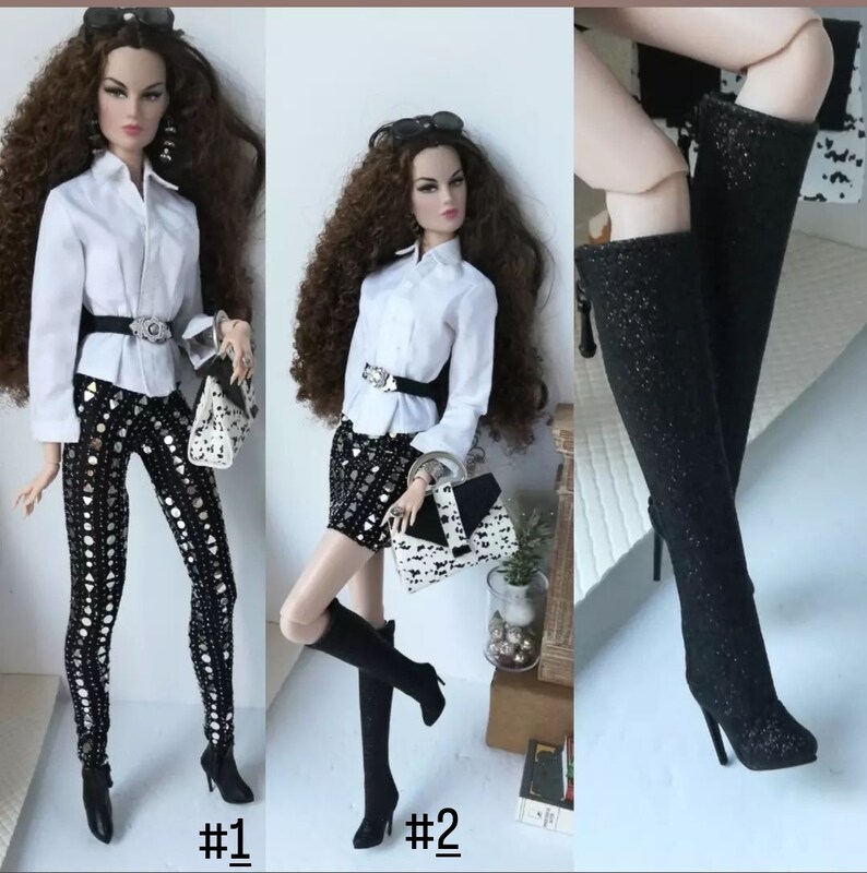 May include: Two fashion dolls wearing white shirts and black boots. The doll on the left is wearing black pants with a silver and black pattern. The doll on the right is wearing a black skirt with a silver and black pattern. Both dolls are holding black and white handbags.