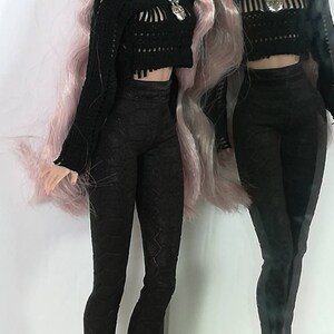 May include: A fashion doll with long pink hair wearing a black crocheted sweater, black trousers, and black boots. The doll is standing in front of a mirror.