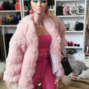 May include: A pink faux fur jacket with a pink sparkly pantsuit. The doll is wearing large red earrings.