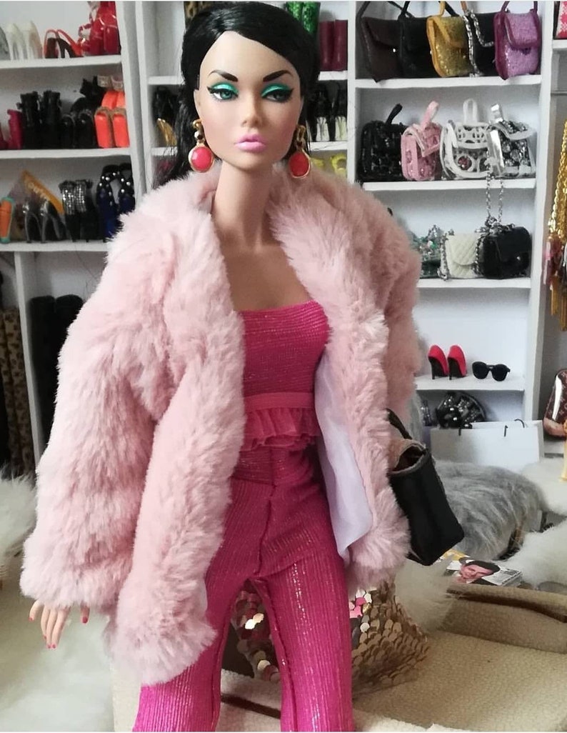 May include: A pink faux fur jacket with a pink sparkly pantsuit. The doll is wearing large red earrings.