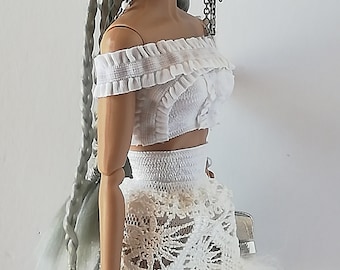 May include: A fashion doll with long silver braids wearing a white off-the-shoulder crop top and a white lace skirt with a white feather trim.