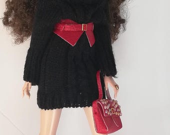 May include: A doll wearing a black sweater dress with a red belt, red sunglasses, and red earrings. The doll is also wearing burgundy knee-high boots and carrying a red handbag with gold accents.