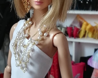 May include: A doll with blonde hair wearing a white one-shoulder dress and a pearl necklace. The doll has gold earrings and is wearing makeup. The doll is standing in front of a shelf with shoes on it.