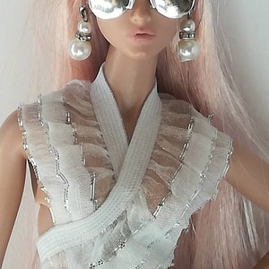 May include: A doll with long pink hair wearing a white ruffled dress, silver mirrored sunglasses, and pearl earrings.