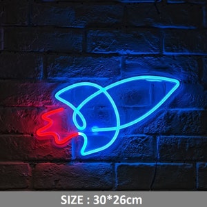 Könnte beinhalten: Ein blaues und rotes Neon-Schild in Form einer Rakete. Das Schild ist an einer Backsteinwand montiert. GRÖSSE: 30*26cm