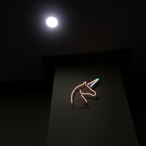 May include: A neon sign of a unicorn head with a rainbow horn against a dark background.