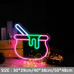 May include: Neon sign shaped like a cauldron with a pink, green, and white outline. The sign is lit up and has a dripping effect. The sign is 30 x 29 cm, 40 x 38 cm, or 50 x 48 cm.