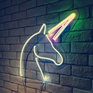May include: A white neon unicorn head sign with a rainbow horn against a brick wall background.