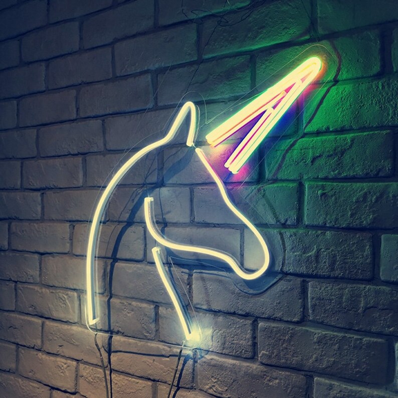 May include: A white neon unicorn head sign with a rainbow horn against a brick wall background.