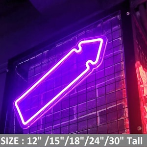 May include: A purple neon arrow sign with a white border, mounted on a black metal grid against a brick wall. The sign's dimensions are listed as 30.5cm, 38cm, 45.7cm, 61cm, and 76cm tall. The text "SIZE: 12" /15"/18"/24"/30" Tall" is at the bottom.
