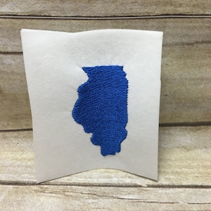 Op de afbeelding: Een blauwe geborduurde omtrek van de staat Illinois op een witte achtergrond.
