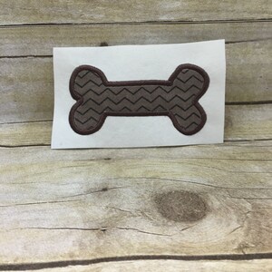 May include: A brown bone-shaped patch with a chevron pattern. The patch is on a white background.