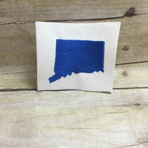 May include: A blue felt outline of the state of Connecticut on a white background.