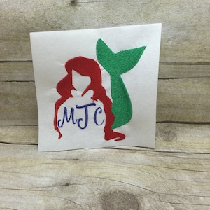 May include: Red and green embroidered design of a mermaid with a tail and the initials "MJC" on a white background.