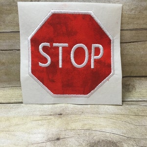 May include: Red and white embroidered stop sign patch. The sign is an octagon shape with white stitching around the edge. The word "STOP" is in white lettering.