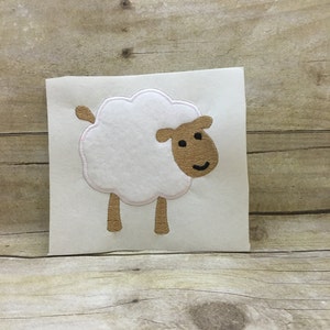 May include: White felt applique of a sheep with brown legs and a brown face. The sheep has a simple smile.