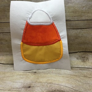 Może przedstawiać: Aplikacja z filcu w kształcie cukrowego kukurydzy z białym wierzchołkiem, pomarańczowym środkiem i żółtym spodem. Aplikacja ma żółty kontur.