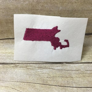 May include: Embroidered patch of the state of Massachusetts in a dark pink color on a white background.