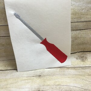 May include: A red and silver screwdriver embroidery design on a white background.