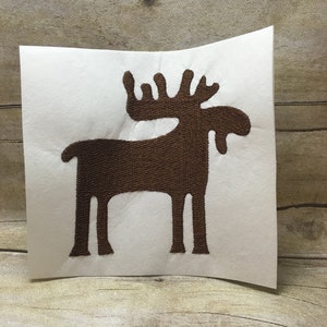 May include: A brown moose silhouette embroidered on a white background.