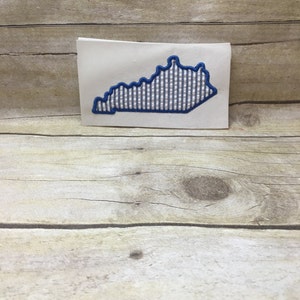May include: A white card with a blue and white gingham outline of the state of Kentucky.
