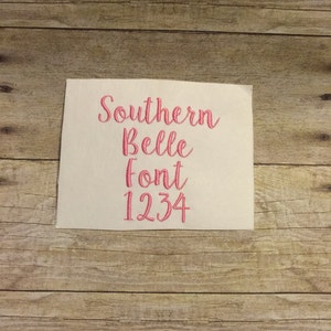May include: A white fabric swatch with pink embroidery that reads "Southern Belle Font 1234".