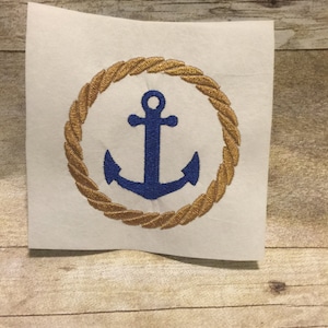 May include: A blue anchor embroidered on a white fabric background with a gold rope circle around it.