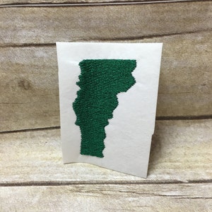 Op de afbeelding: Een groene vilt omtrek van de staat Vermont op een witte achtergrond.