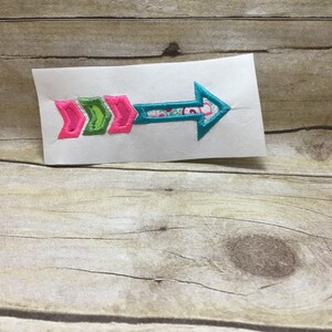 May include: A turquoise, pink, and green arrow embroidered patch. The arrow is pointing to the right.