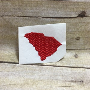 May include: Red embroidered outline of the state of South Carolina on a white background.