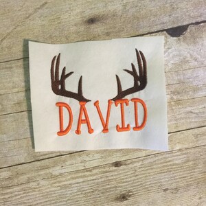 May include: Embroidered design featuring a pair of brown antlers and the name "DAVID" in orange thread.