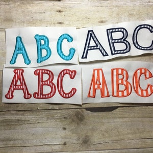 May include: Four sets of iron-on letters in different colors and patterns. The letters are "ABC" in blue and white stripes, red and white stripes, orange and white stripes, and navy blue and white stripes.